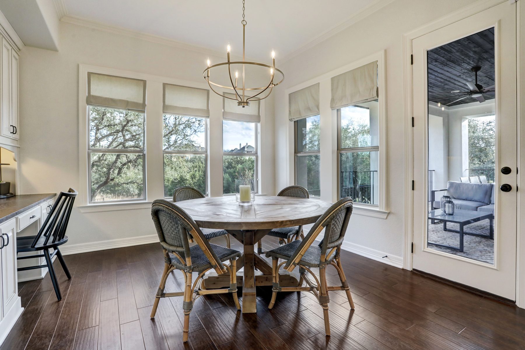 Breakfast nook with a round reclaimed wood table, rattan bistro chairs and a brass chandelier