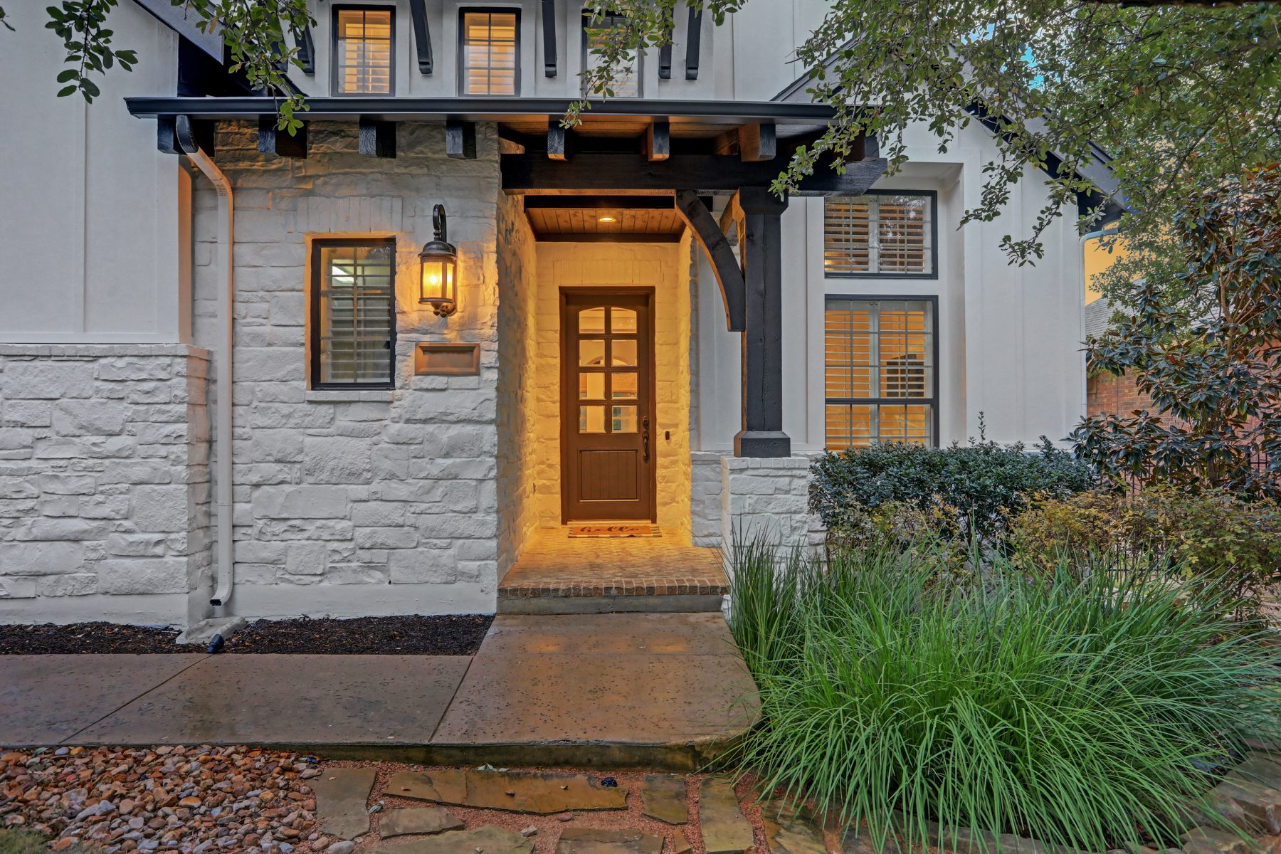 Stone and board-and-batten home entry with a lantern-lit wood door at dusk