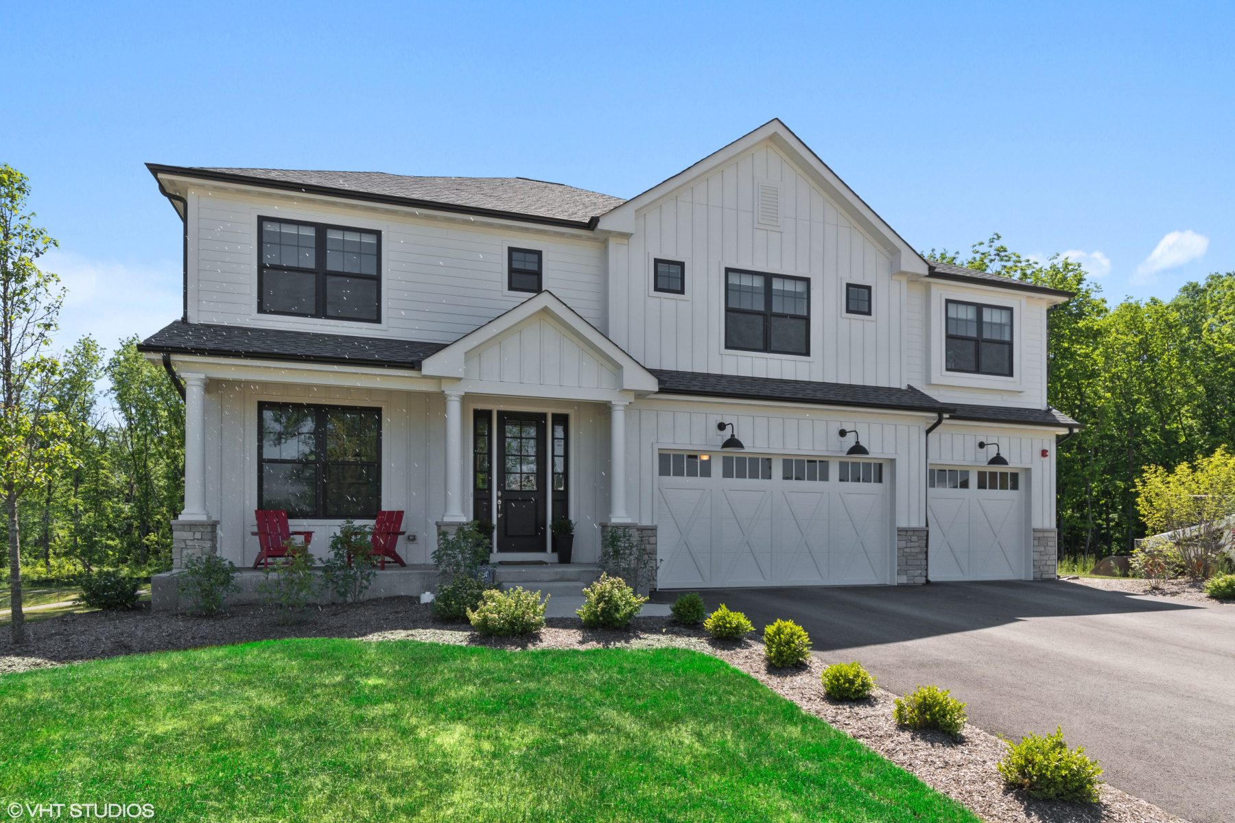 White modern farmhouse with board-and-batten siding, black windows, a covered front porch and a three-car garage