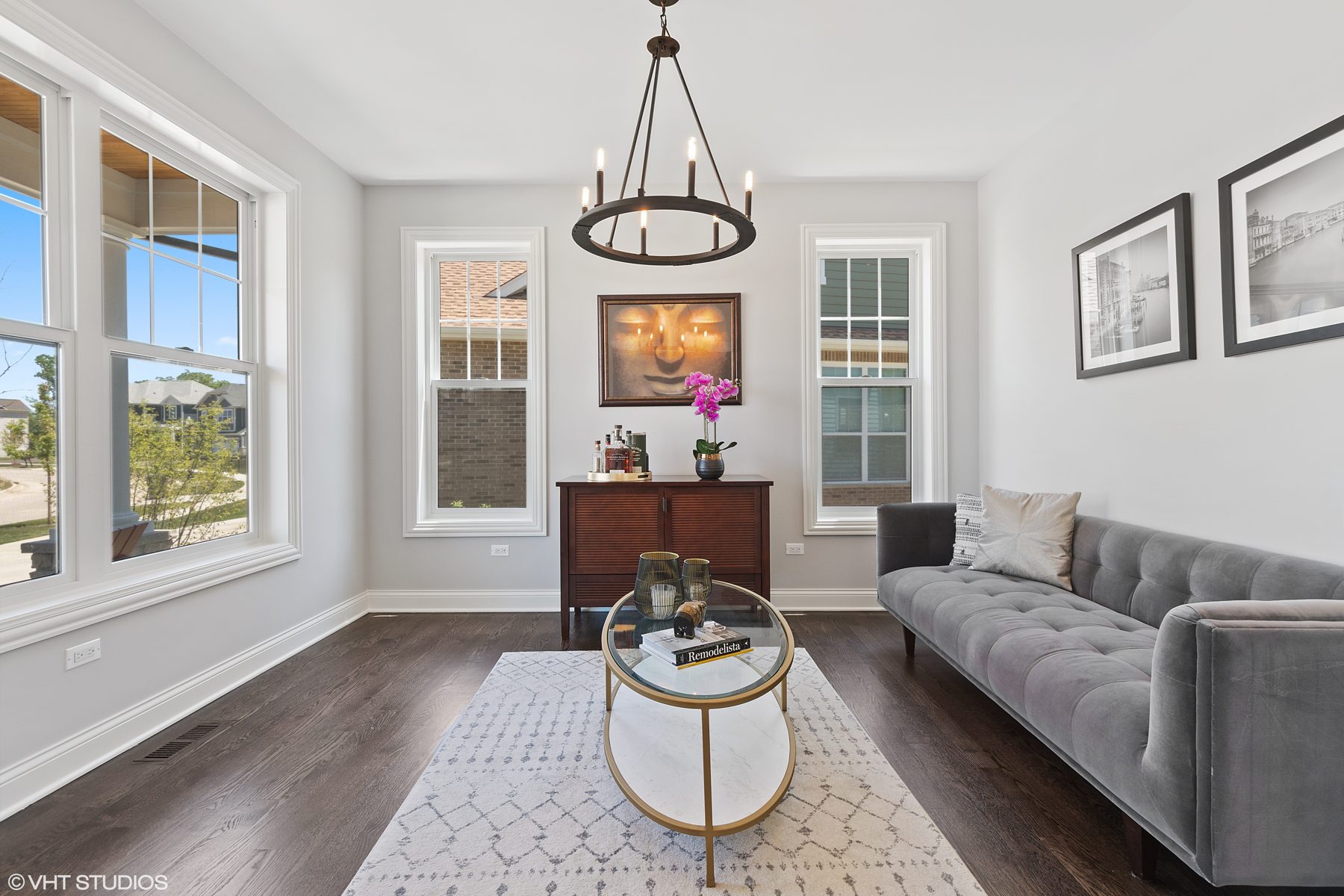 Front study with a wrought-iron chandelier, gray velvet sofa and glass and brass coffee table